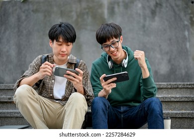 Happy young Asian man college student playing mobile game on his smartphone with his friend at campus building stairs. hobby and leisure concept - Powered by Shutterstock