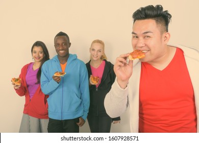 Happy Young Asian Man Eating Slice Of Pizza With Diverse Group Of Multi Ethnic Friends Smiling And Holding Slice Of Pizza Together