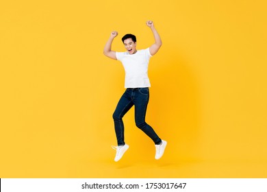 Happy Young Asian Man Jumping With Hands Up Isolated On Yellow Background