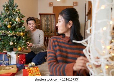 Happy Young Asian Man Putting Glowing Lights On Christmas Tree