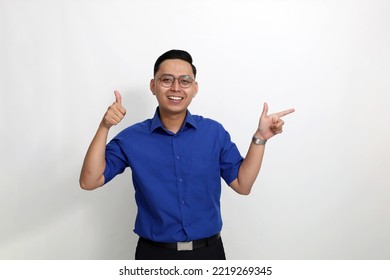 Happy Young Asian Man Standing While Pointing Sideways And Showing Thumbs Up. Isolated On White