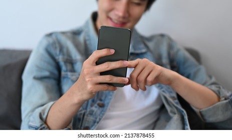 Happy Young Asian Man Texting Message, Surfing Web On Smart Phone At Home.