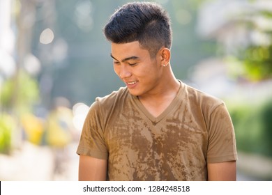 Happy Young Asian Man Thinking And Looking Down Outdoors