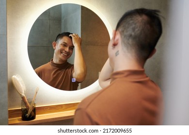 Happy Young Asian Man Touching His Hair When Looking At Bathroom Mirror