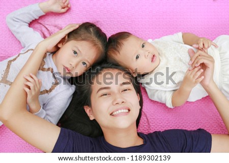 Happy Young Asian mother daughter and son lying on pink mattress mat looking at camera. View from above.
