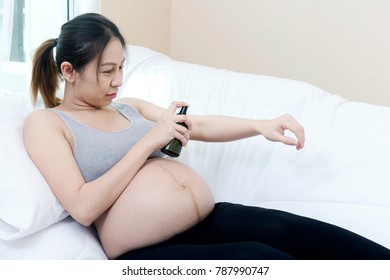 Happy Young Asian mother or pregnant woman using Spraying Mineral Water or Perfume while sitting on sofa at home in bedroom. Treatment, Skin, Beauty, Cosmetic, Makeup, Healthy, Lifestyle concept.