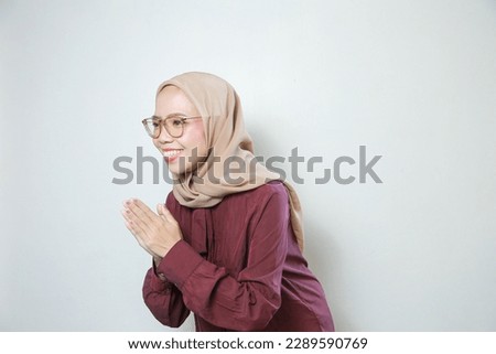 Happy young Asian Muslim woman wearing glasses greeting with both hands isolated over white background