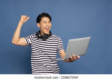 Happy young Asian pro gamer with headphones holding computer laptop and win in online video game isolated over blue background, Cyber sportsman playing tournaments concept - Powered by Shutterstock