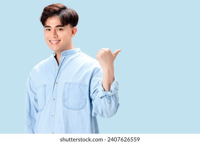 Happy young Asian smart man pointing thumb to copy space over isolated blue background. - Powered by Shutterstock