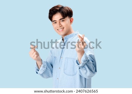 Happy young Asian smart man showing hand signal mini heart over isolated blue background.