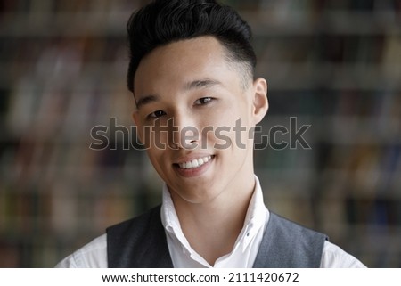Happy young Asian student guy head shot portrait. Cheerful confident young man with trendy hairstyle wearing formal cloth, looking at camera with toothy smile. Male head shot portrait