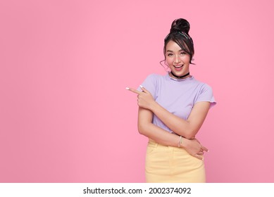 Happy young Asian teen woman standing with her finger pointing isolated on pink background with copy space. 