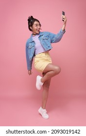 Happy young asian teen woman celebrating with mobile phone isolated over pink background.
