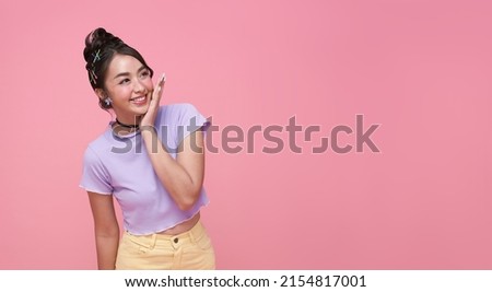 Happy young Asian teen woman looking at copy space on pink background.