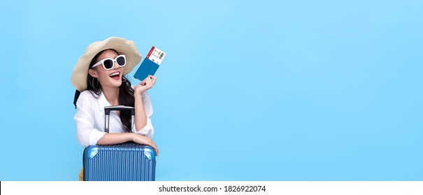 Happy young Asian tourist woman holding passport and boarding pass with baggage going to travel on holidays on blue background. - Powered by Shutterstock