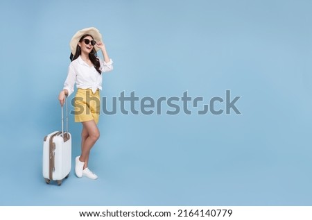 Happy young Asian tourist woman holding baggage going to travel on holidays isolated on blue background. copy space