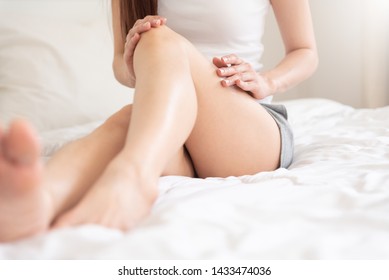 Happy Young Asian woman applying body lotion on her legs at her bedroom. Body care and Health.