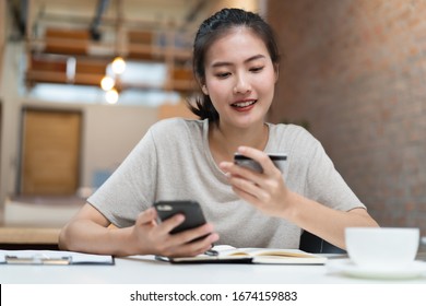 Happy Young Asian Woman Buying Stuff From Online Retail And Paying Bills Via Banking Application. Girl Looking At Credit Card In Her Hand And Fill Data To Mobile Phone To Complete Purchese Order..