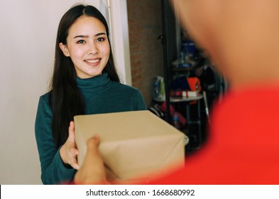 Happy Young Asian Woman Customer Smiling Receive Parcel Post Box From Home Delivery Service Man In Red Uniform At Home, Express Home Delivery Service, Logistics Shipping And Online Shopping Concept