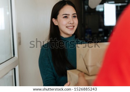 happy young asian woman customer smiling receive parcel post box from home delivery service man in red uniform at home, express home delivery service, logistics shipping and online shopping concept