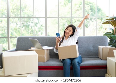 Happy Young Asian Woman Entrepreneur, Smile For Sales Success After Checking Order From Online Shopping Store In A Smartphone At Home Office, Concept Of Merchant Business Online And ECommerce