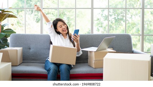 Happy Young Asian Woman Entrepreneur, Smile For Sales Success After Checking Order From Online Shopping Store In A Smartphone At Home Office, Concept Of Merchant Business Online And ECommerce