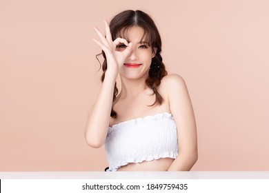 Happy young asian woman has two pigtails smiles and showing OK sign, Presenting your product. Clean and fresh skin with positive emotional, Facial treatment, isolated on beige background.