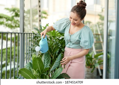 Happy Young Asian Woman Housewife Watering Flowers On Balcony.