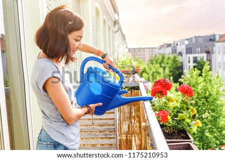 Happy Young Asian Woman housewife Watering flowers On Balcony