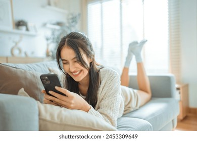 Happy young asian woman lady browsing surfing wireless internet on mobile phone while sitting a sofa couch in living room at home apartment, Shopping online via website - Powered by Shutterstock