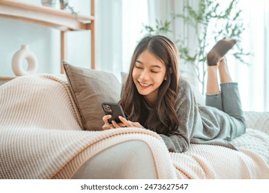 Happy young asian woman lady browsing surfing wireless internet on mobile phone while sitting a sofa couch in living room at home apartment, Shopping online via website - Powered by Shutterstock