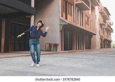 Happy Young Asian Woman Listening To Music And Having Fun With Headphones Via Smartphone On The Street.