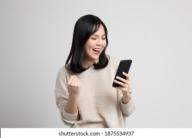 Happy young asian woman looking at screen of smartphone standing on isolated white background. She very happy.