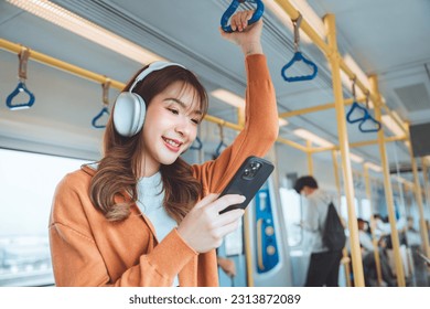 Happy young Asian woman passenger listening music via smart mobile phone in a train, Smile female wearing wireless headphones while moving in the tram, lifestyle, transportation. - Powered by Shutterstock