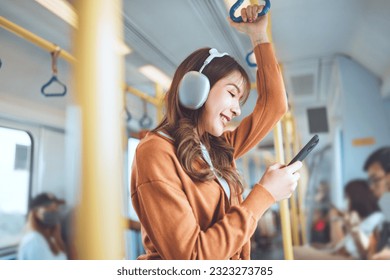 Happy young Asian woman passenger listening music via smart mobile phone in a train, Smile female wearing wireless headphones while moving in the tram, lifestyle, transportation. - Powered by Shutterstock