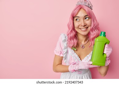 Happy Young Asian Woman With Pink Dyed Hair Dressed Like Housemaid Advertises Detergent For Cleaning Smiles Gladfully Looks Aside Isolated Over Rosy Background Blank Space For Your Promotion