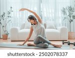 Happy young Asian woman practicing yoga and shoulder stretching at home sitting on floor in living room