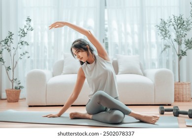 Happy young Asian woman practicing yoga and shoulder stretching at home sitting on floor in living room - Powered by Shutterstock