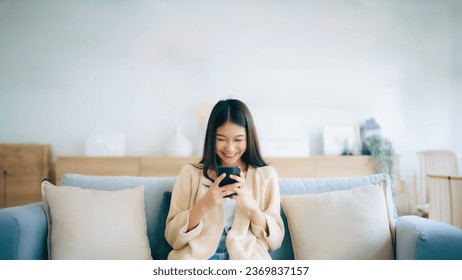 Happy young asian woman relax on comfortable couch at home texting messaging on smartphone, smiling girl use cellphone, chatting online message, shopping online from home - Powered by Shutterstock