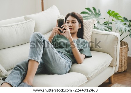 Happy young asian woman relaxing at home. Female is lying down on sofa and using mobile smartphone 商業照片 © 