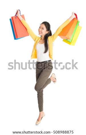 Happy young Asian woman shopper jumping, hands outstretched holding shopping bags and smiling, full length isolated standing on white background.