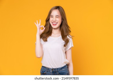 Happy young Asian woman shows ok sign on yellow background.