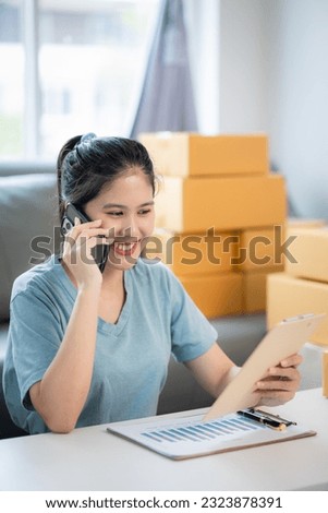 Happy young asian woman smiling at sales success after checking order from online store on smartphone at home office The concept of online commerce and e-commerce.