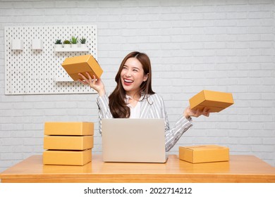 Happy young asian woman startup small business freelance holding parcel box and computer laptop and sitting on chair, Online marketing packing box delivery concept - Shutterstock ID 2022714212