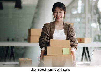 Happy Young Asian Woman Startup Small Business Freelance Holding Parcel Box And Computer Laptop. Online Marketing Packing Box Delivery Concept
