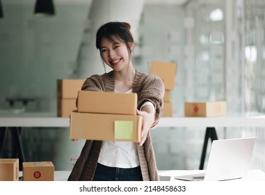 Happy Young Asian Woman Startup Small Business Freelance Holding Parcel Box And Computer Laptop. Online Marketing Packing Box Delivery Concept
