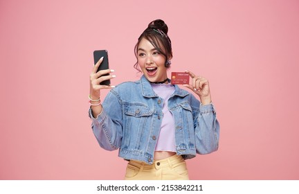 happy young asian woman using mobile phone and credit card isolated over ping background.