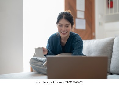 Happy Young Asian Woman Using Laptop Computer On Cozy Sofa, Sunday Morning Concept