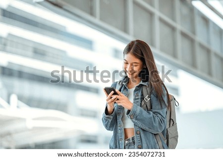 Happy young asian woman using social media on mobile phone in a urban city. Smiling female checking message on mobile phone in town.