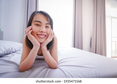 Happy young Asian woman waking up on her bed